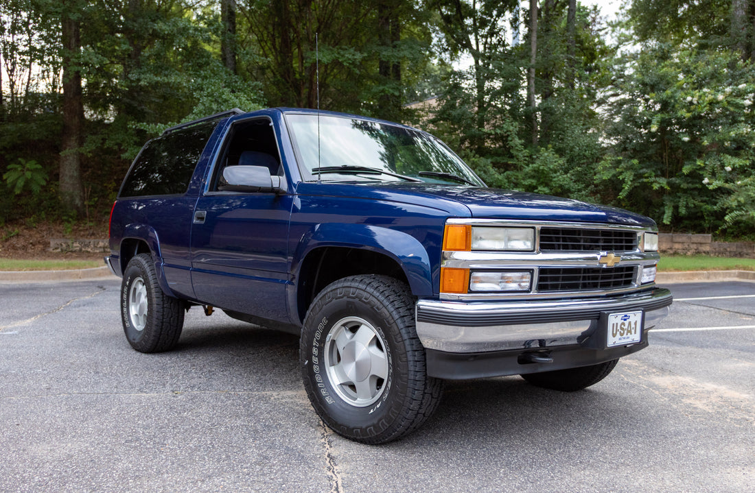 A dark blue Chevrolet Tahoe SUV parked on an asphalt surface with a background of green trees.
